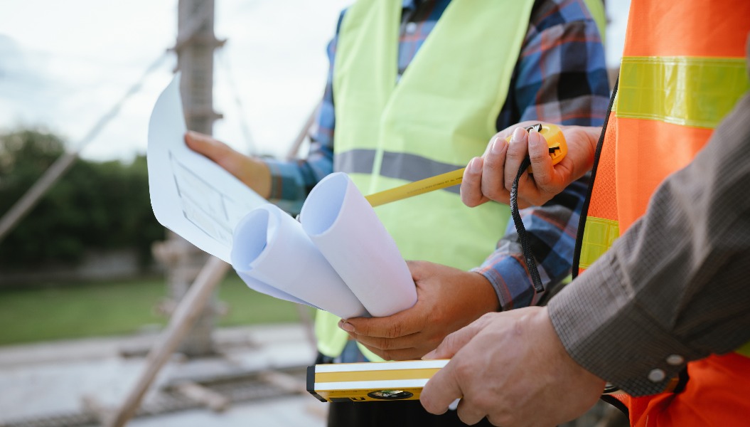 Ein Bauarbeiter inspiziert einen Betonpfeiler mit einer Wasserwaage, um Präzision und Qualitätskontrolle während der strukturellen Entwicklung in einem städtischen Bauprojekt unter professioneller Aufsicht zu gewährleisten.