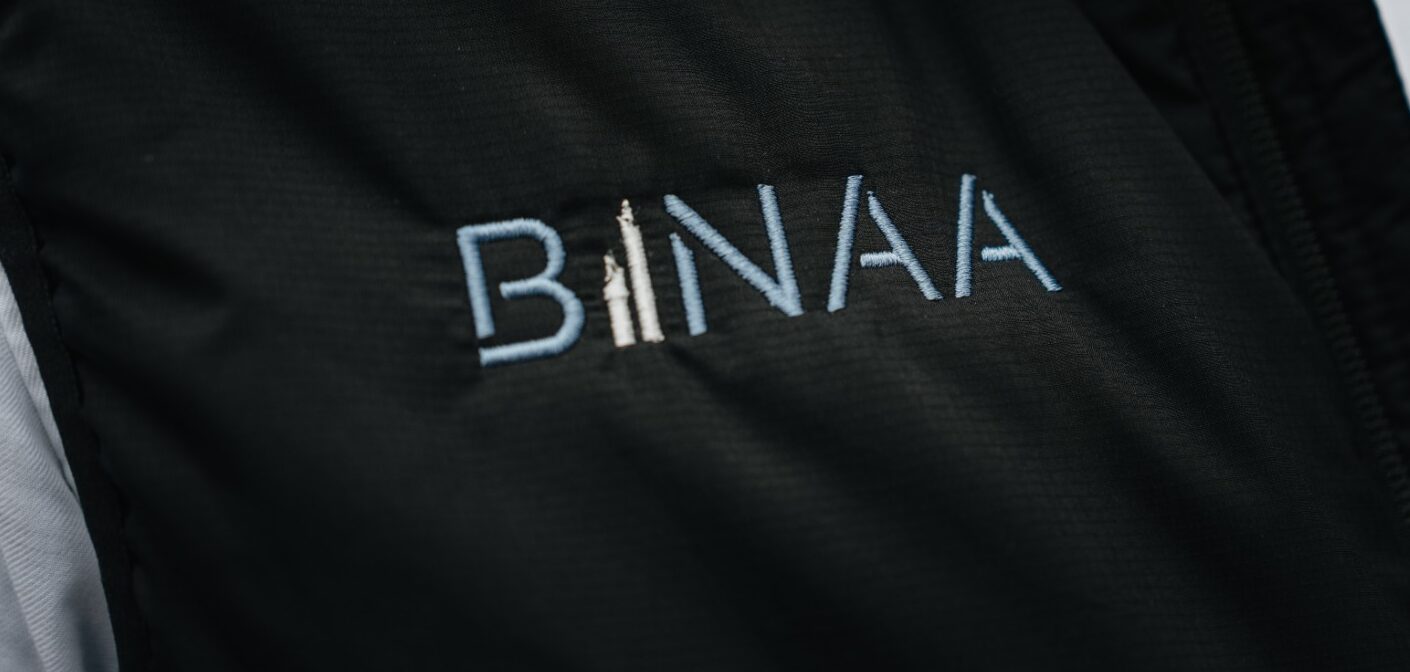 Schwarze Jacke mit heller Stickerei des Schriftzugs BINAA ueber weissem Hemd