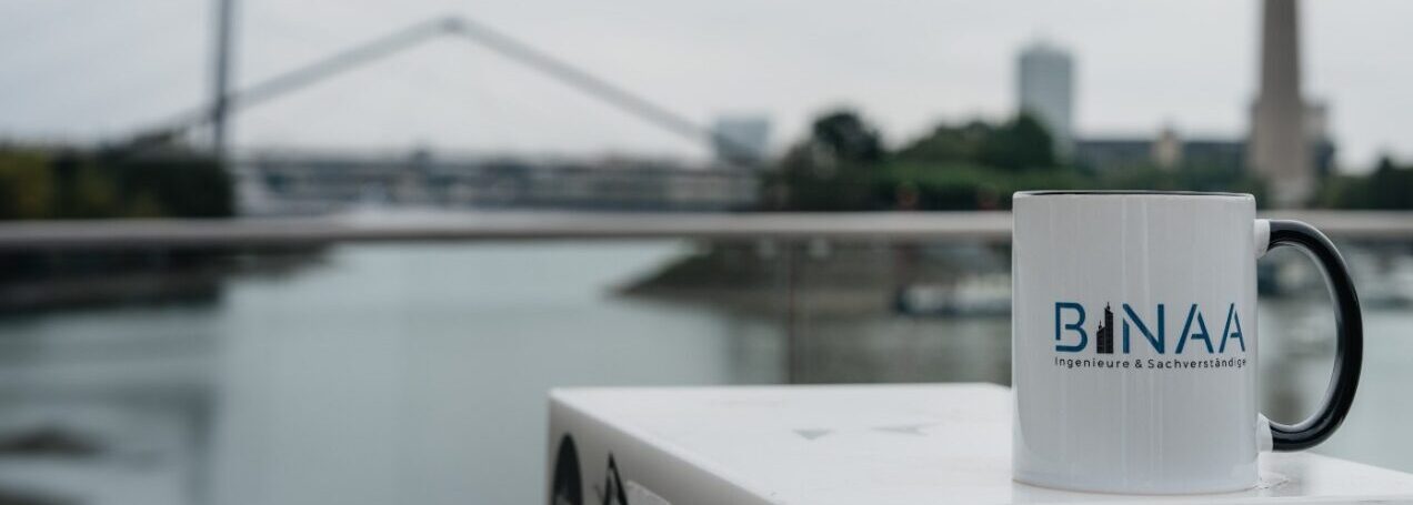 Weisse BINAA Tasse vor dem Duesseldorfer Rheinturm am bewoelkten Himmel